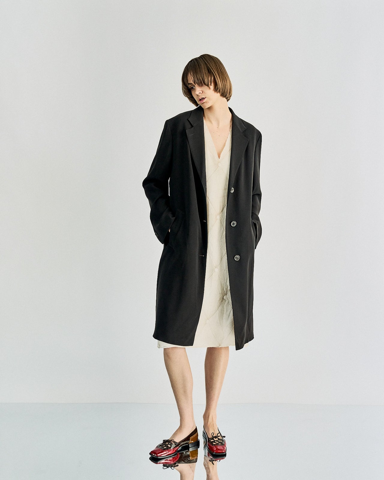 A knee-length black Maison Margiela coat with a notch lapel and three-button closure, featuring two external pockets and fully lined interior.
