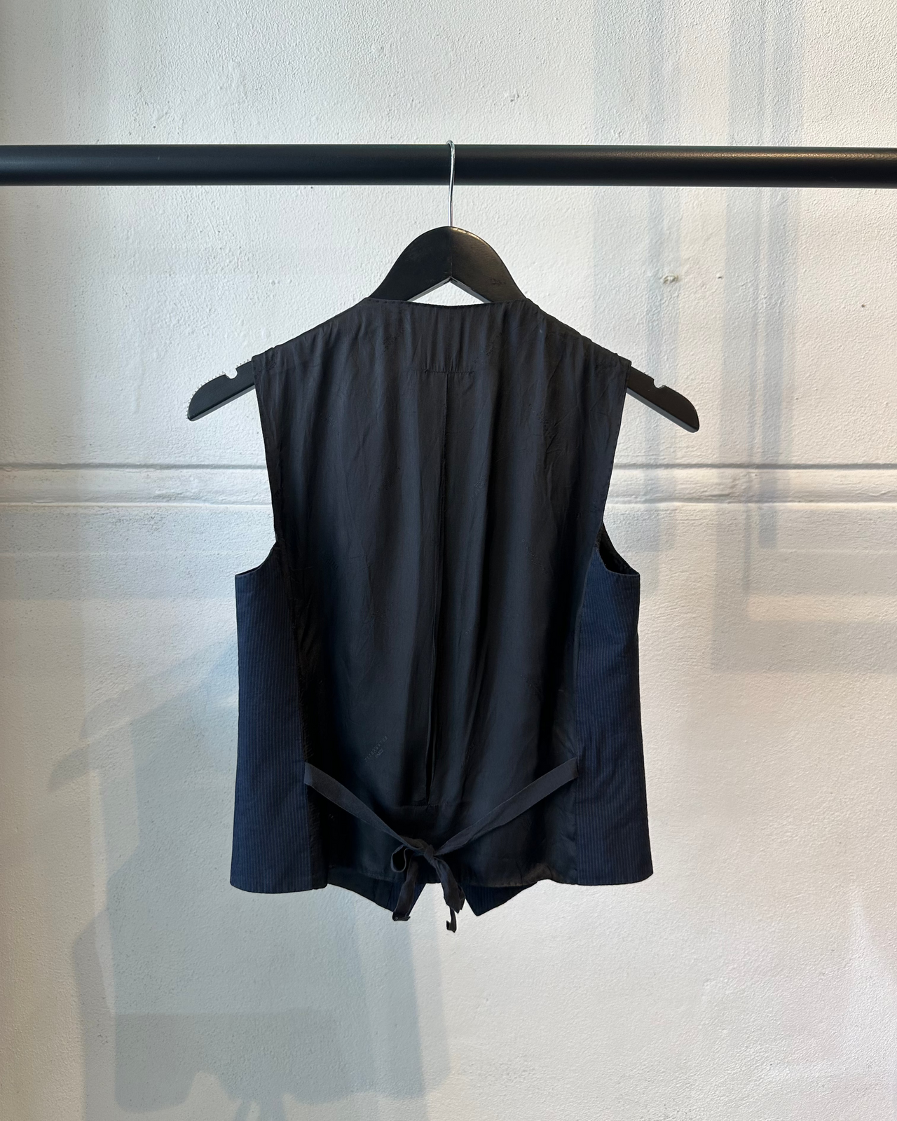 Navy blue vest Maison Margiela with buttons on a hanger against a light gray wall.