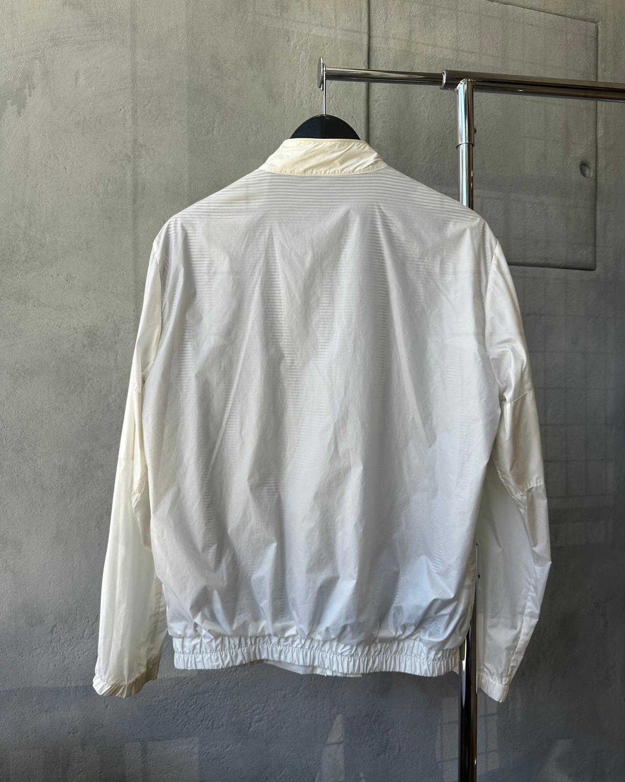 White Maison Margiela jacket on a hanger against a gray concrete wall