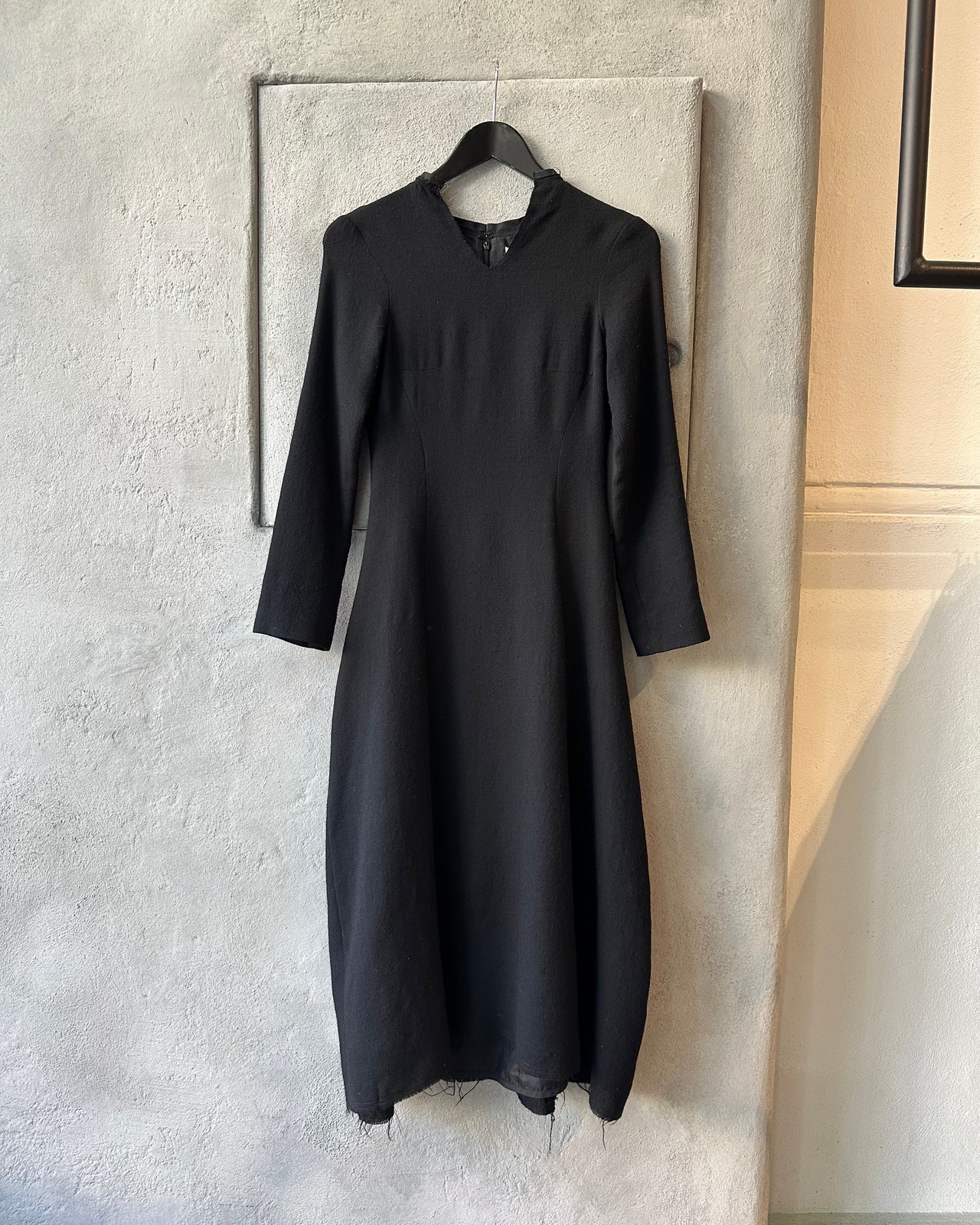 Black Marc Le Bihan dress hanging on a hanger against a neutral wall.
