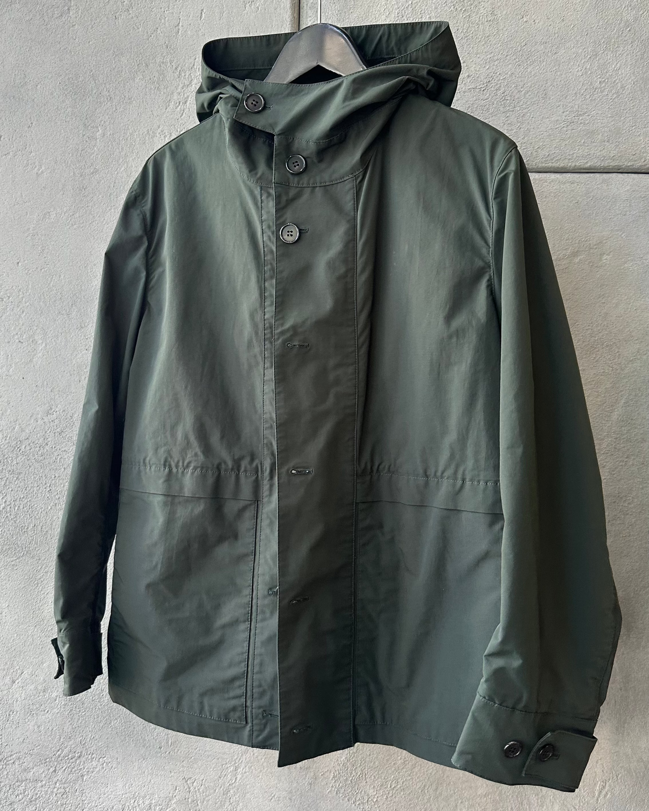 Green Marni raincoat hanging on a rack against a gray wall
