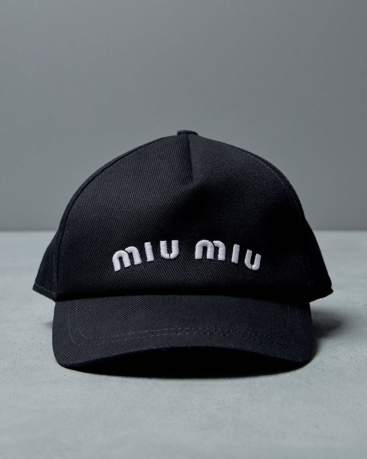 Black cap with 'miu miu' branding on a gray background