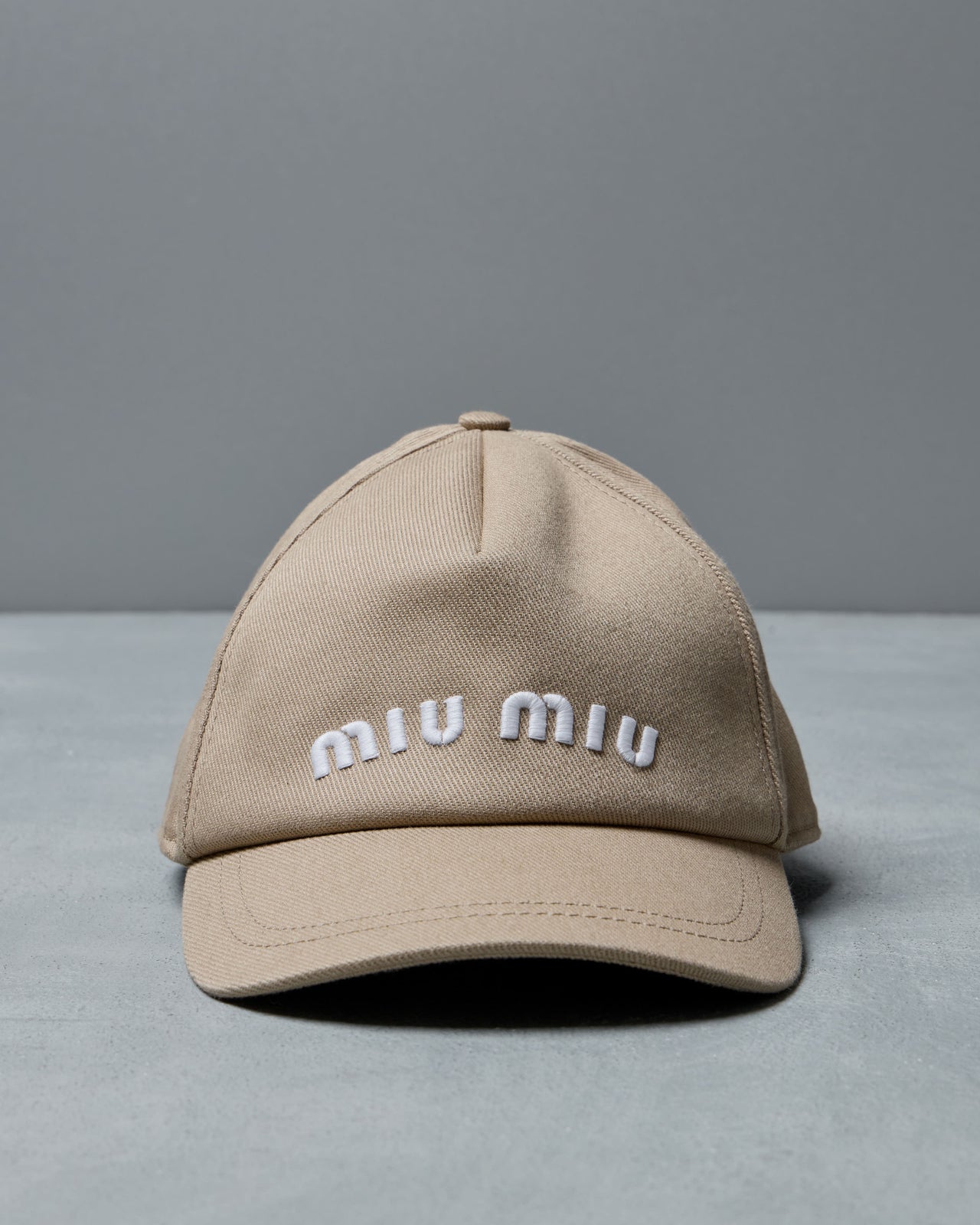 Beige cap with 'miu miu' logo on a gray background