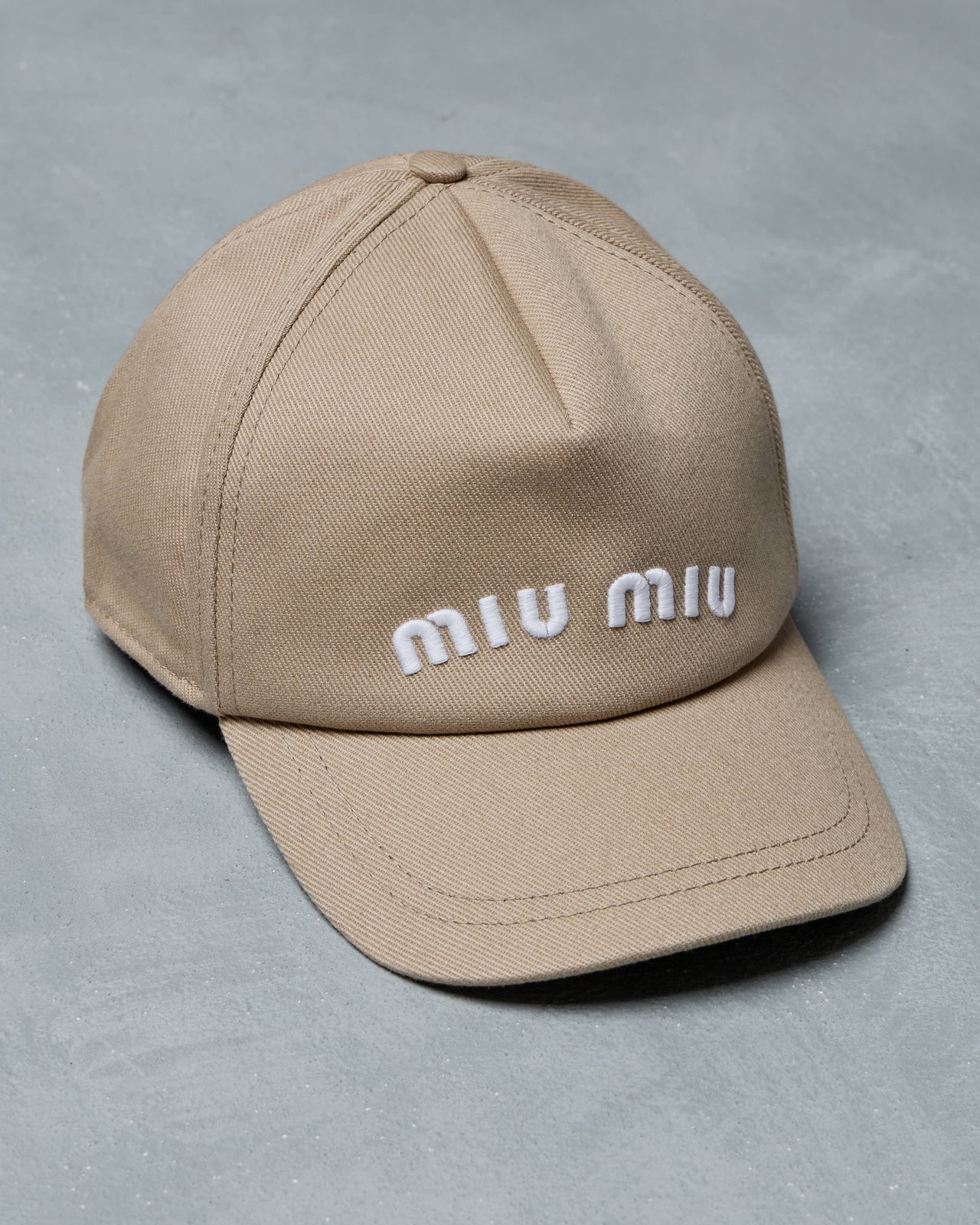Beige cap with 'miu miu' logo on a gray background