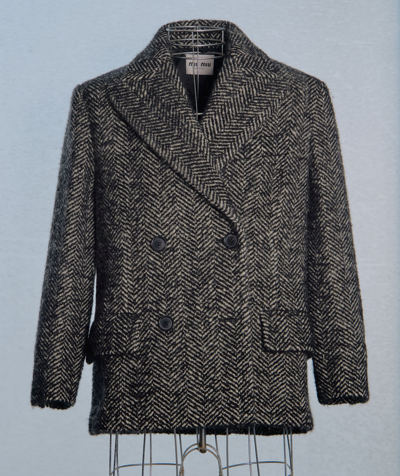 Herringbone Miu Miu patterned coat on a mannequin against a light blue background