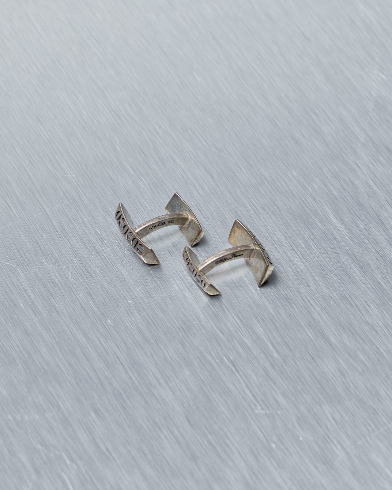 Silver open-style Tiffany and Co cufflinks on a textured gray background