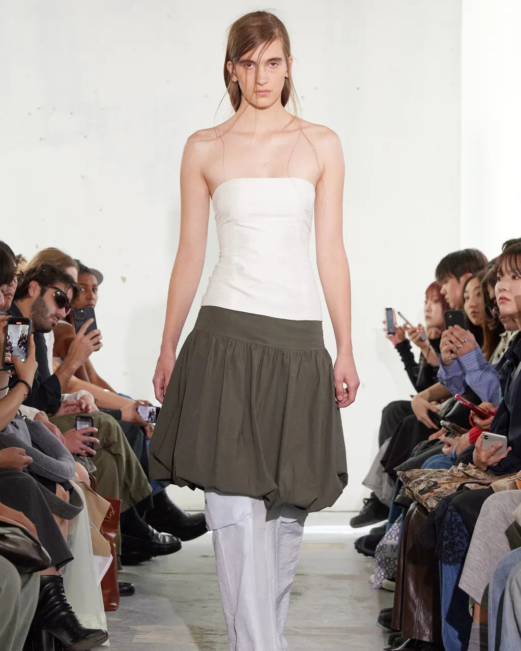 Model walking down a runway wearing a strapless white top and green Paloma Wool skirt.