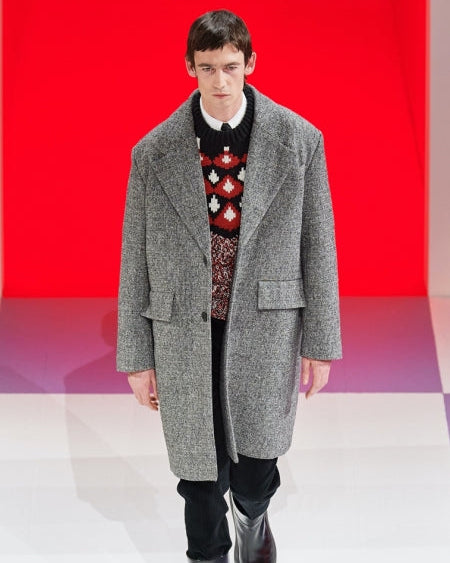 Man wearing a gray coat over a colourful Prada sweater on a red and white checkered background
