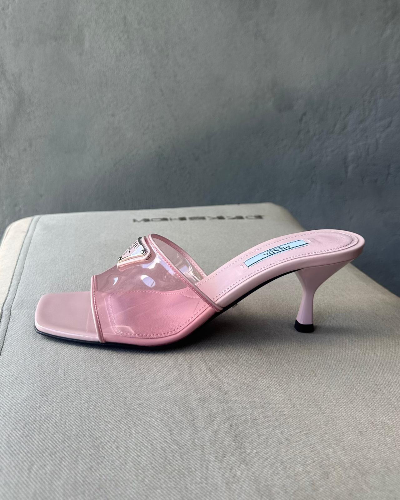 Pink high-heeled Prada shoe on a textured surface with a gray background