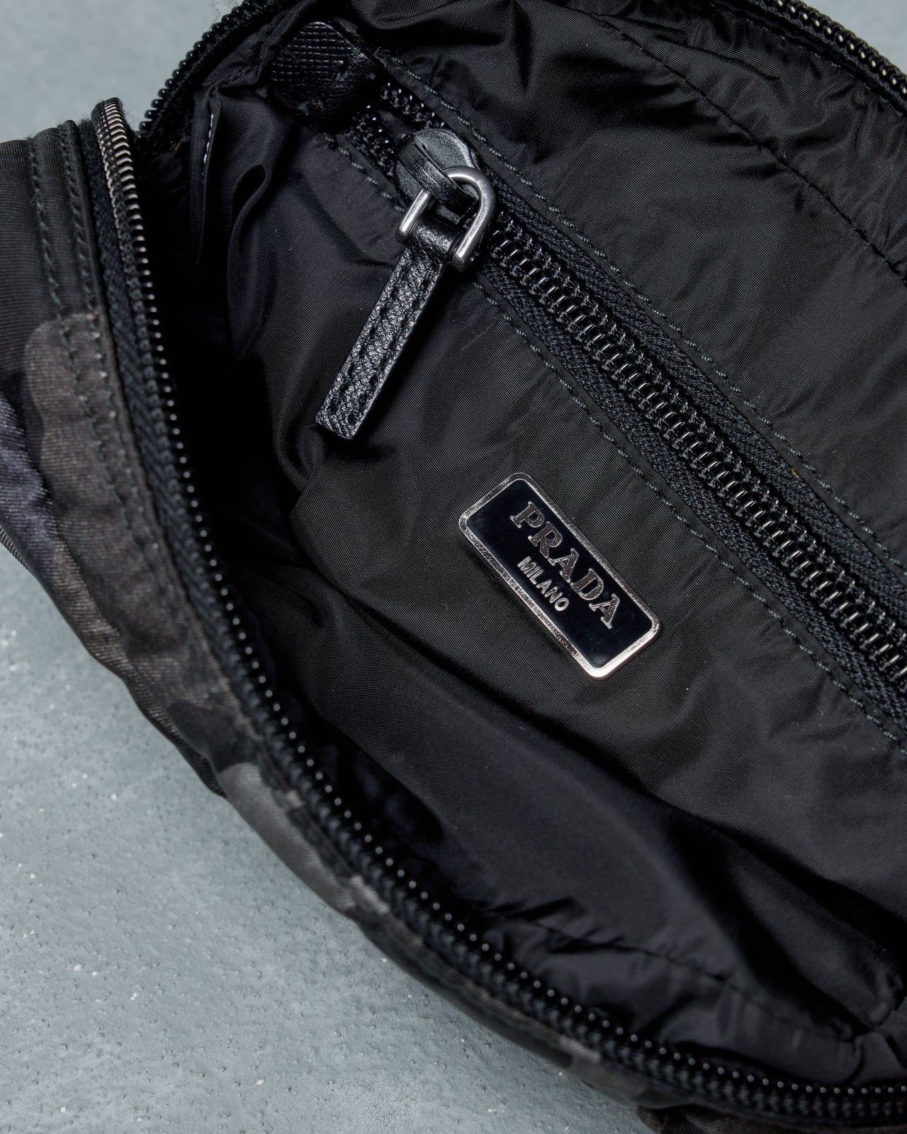 Prada Camouflage-patterned pouch with a brand logo on a gray background