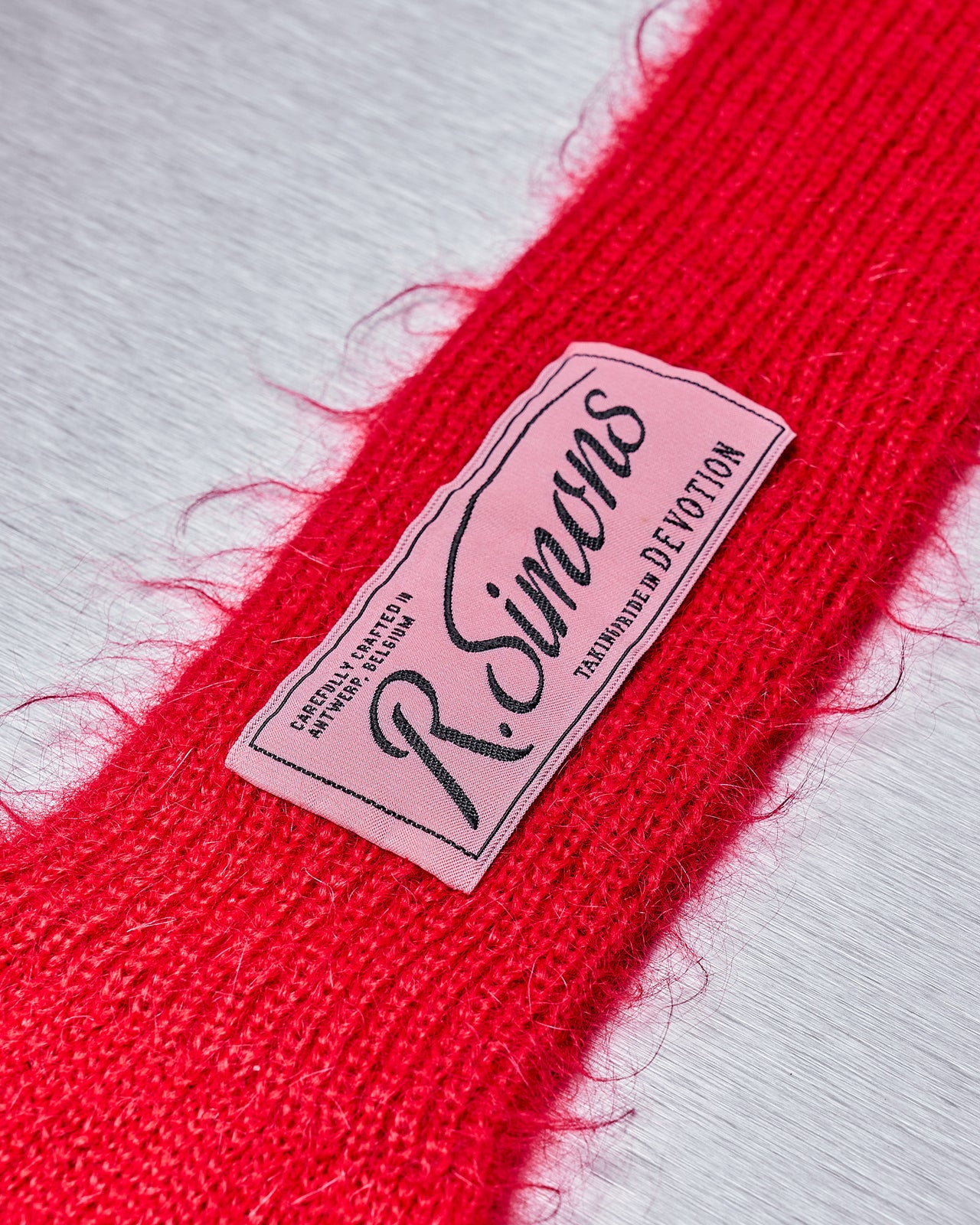 A pair of red wool Raf Simons opera gloves with ribbed cuffs and a branded patch on the wrist.