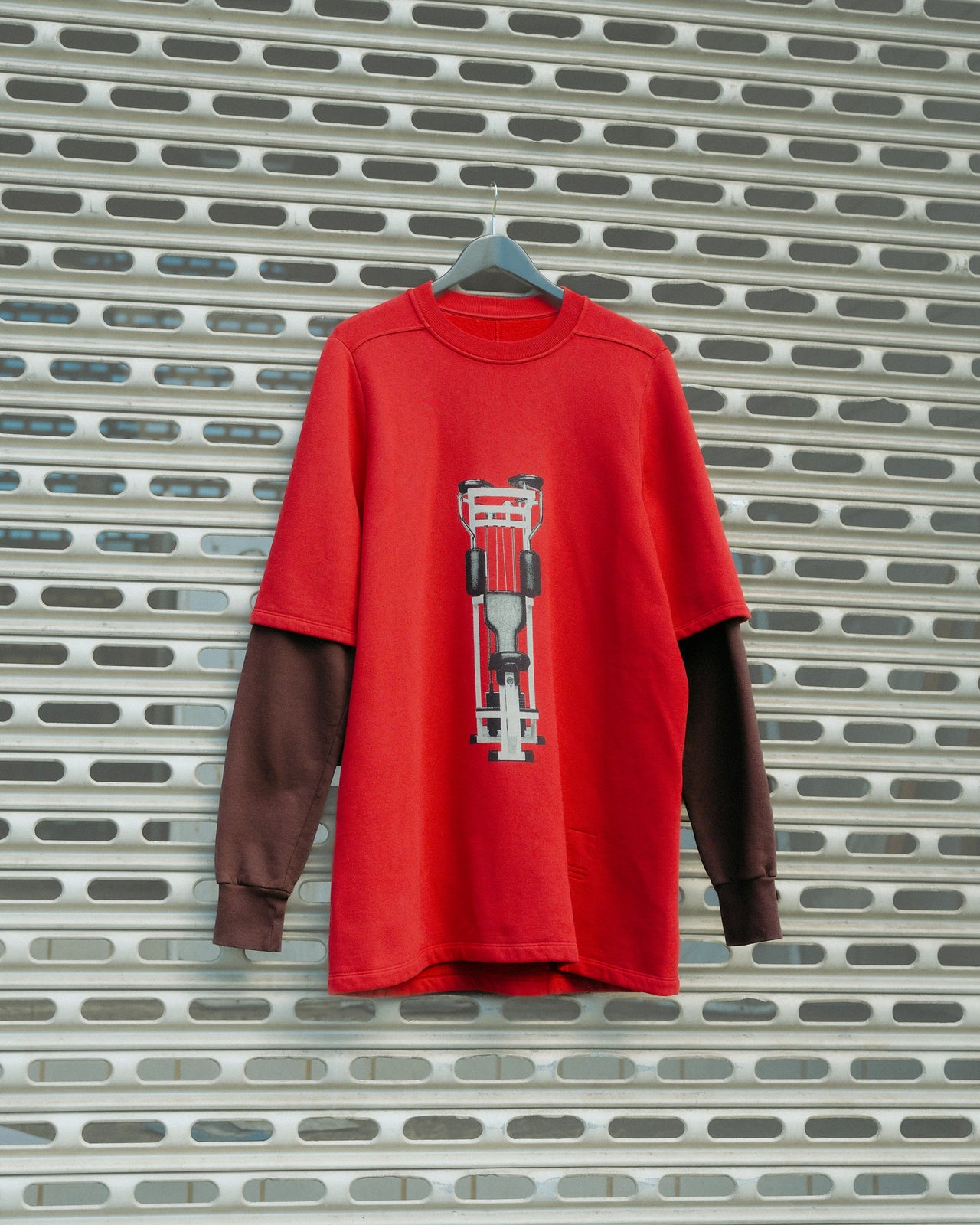 Red and brown layered Rick Owens T-shirt on a hanger with a race car design, set against a metal grill background, creating a modern and sporty vibe.