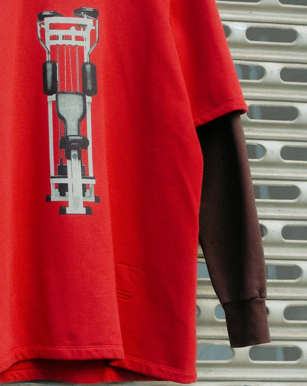 Red and brown layered Rick Owens T-shirt on a hanger with a race car design, set against a metal grill background, creating a modern and sporty vibe.