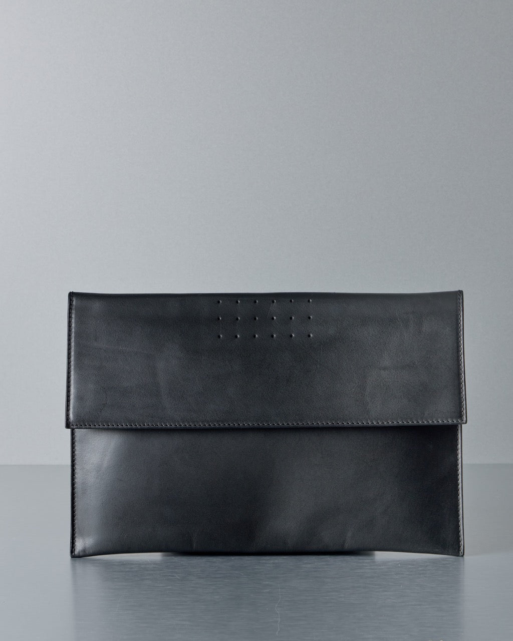Black leather Rick Owens clutch bag on a gray surface with a light gray background
