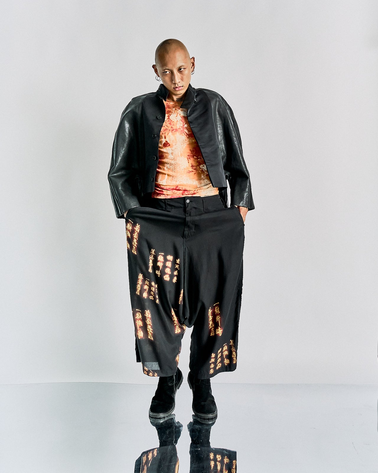 A model wearing a Rick Owens FW 2012 Mountain leather Geoshield jacket, featuring a collar, satin panelling, and leather stripe detailing on the sleeves. The jacket is black with a sculpted fit and exaggerated round shoulders.