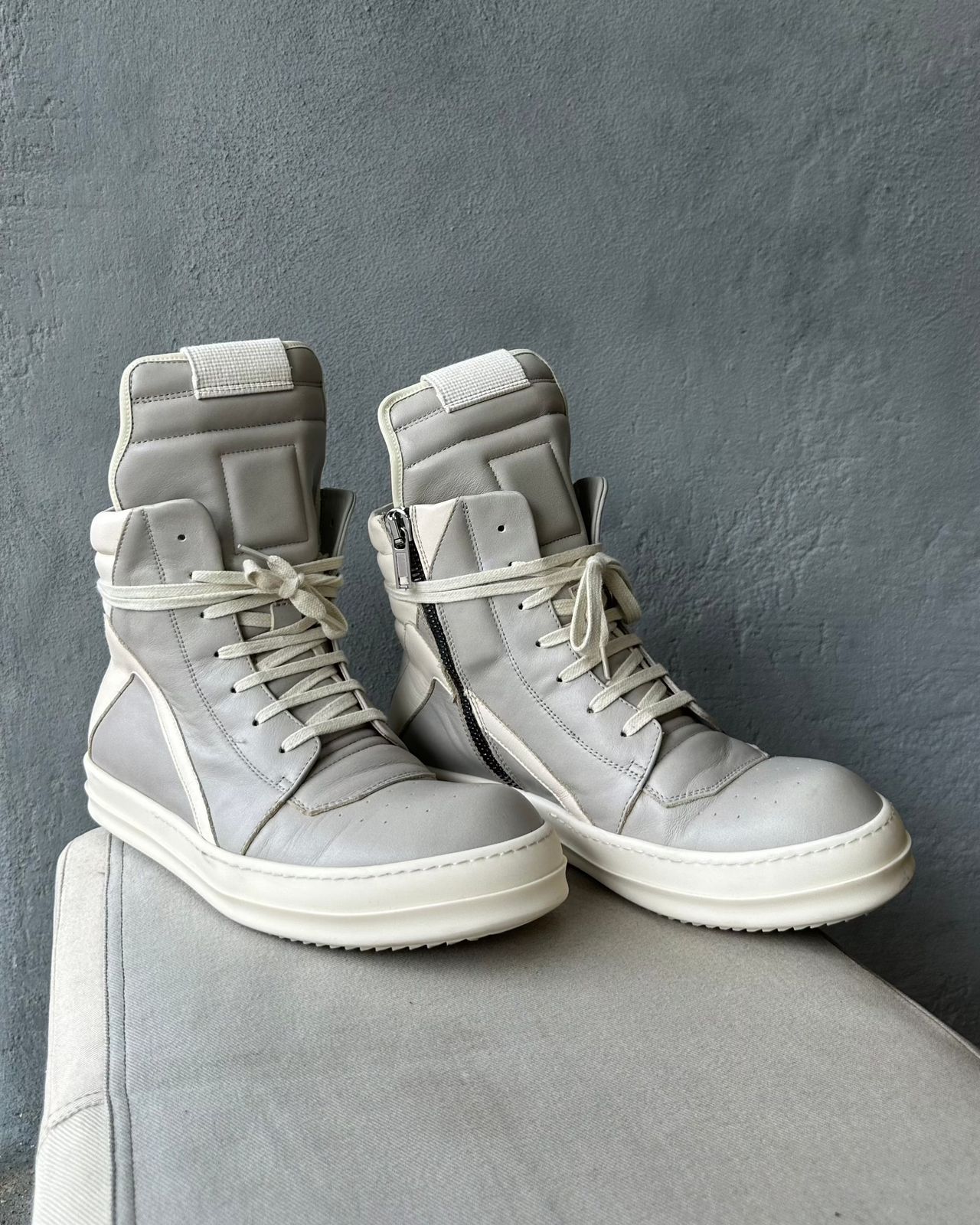 Gray high-top Rick Owens sneaker with white sole on a gray surface against a gray background