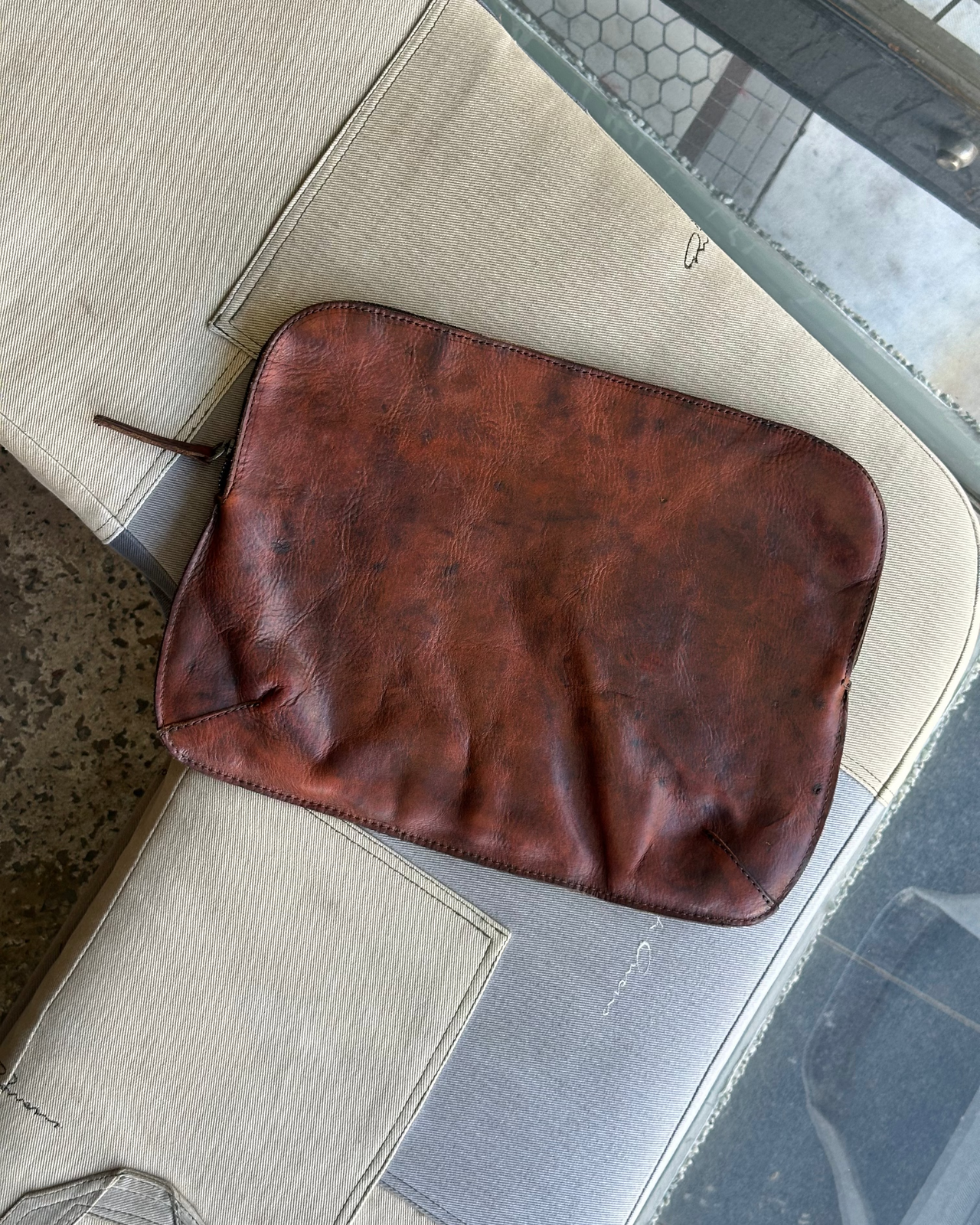 Brown leather Royal Republiq pouch hanging on a hook against a gray wall