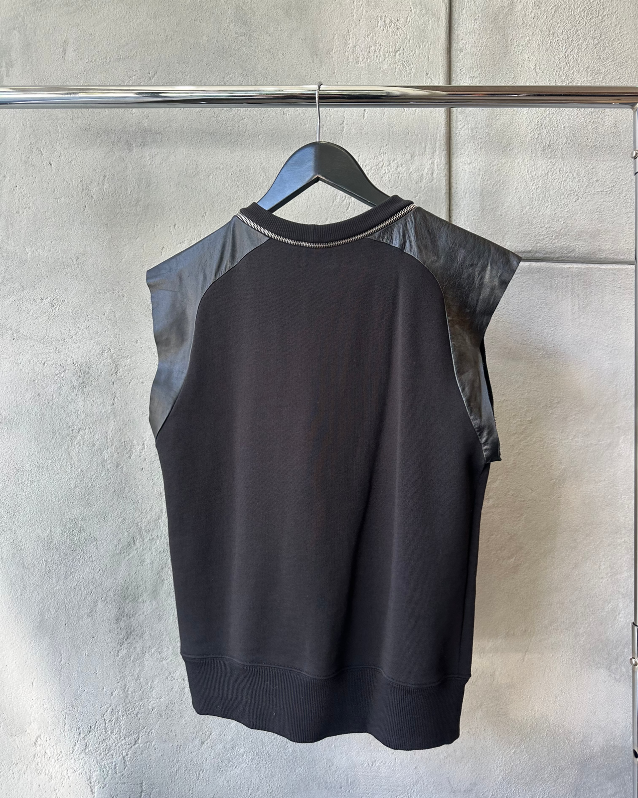 Black sleeveless Saint Laurent top with leather sleeves on a hanger against a gray wall.