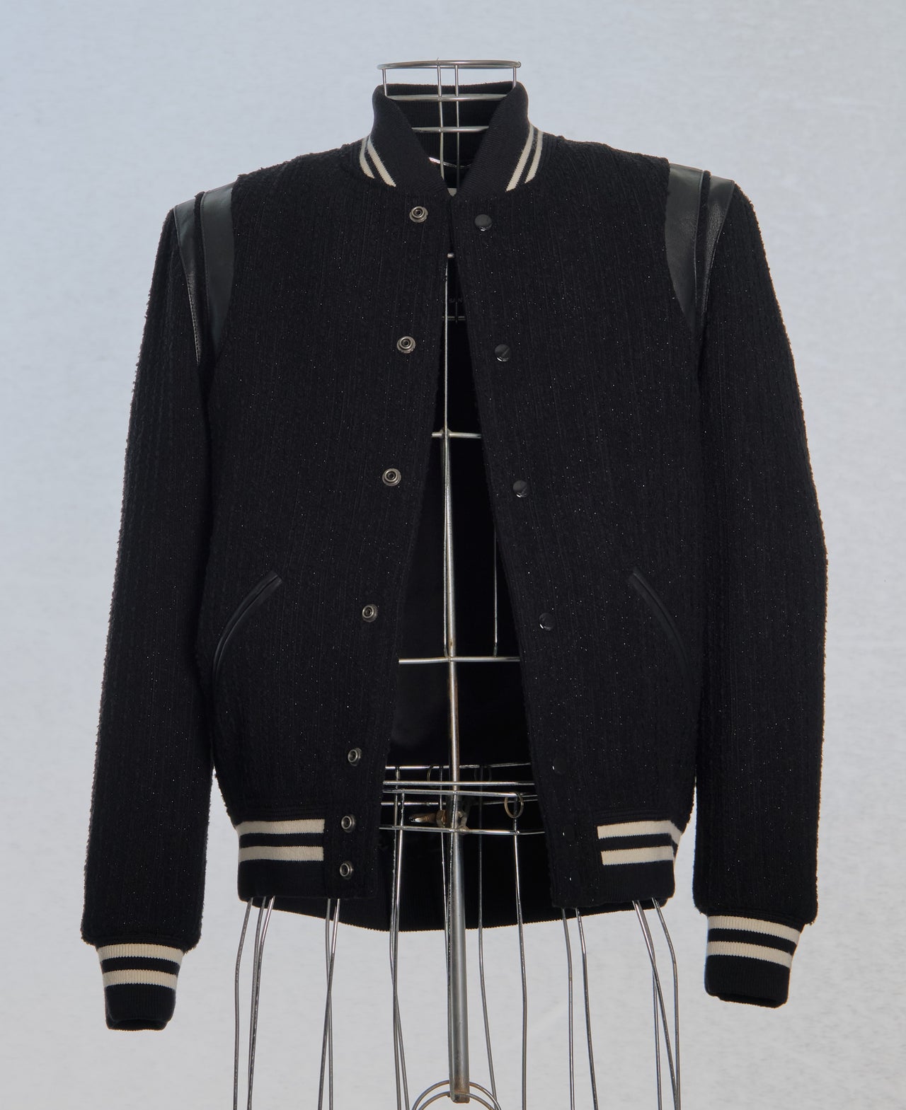 Black Saint Laurent varsity jacket with white accents on a mannequin against a light gray background