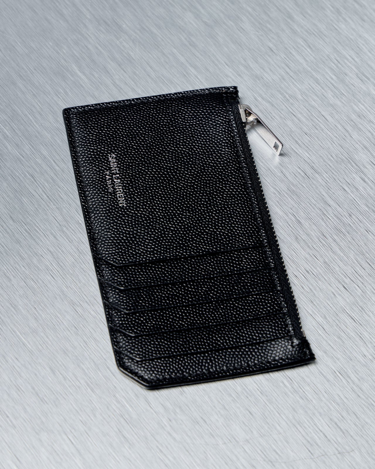 Black Saint Laurent leather wallet with a brand logo on a gray textured surface