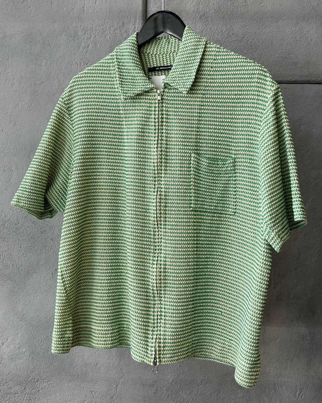 Green checkered Song For The Mute shirt on a hanger against a gray wall