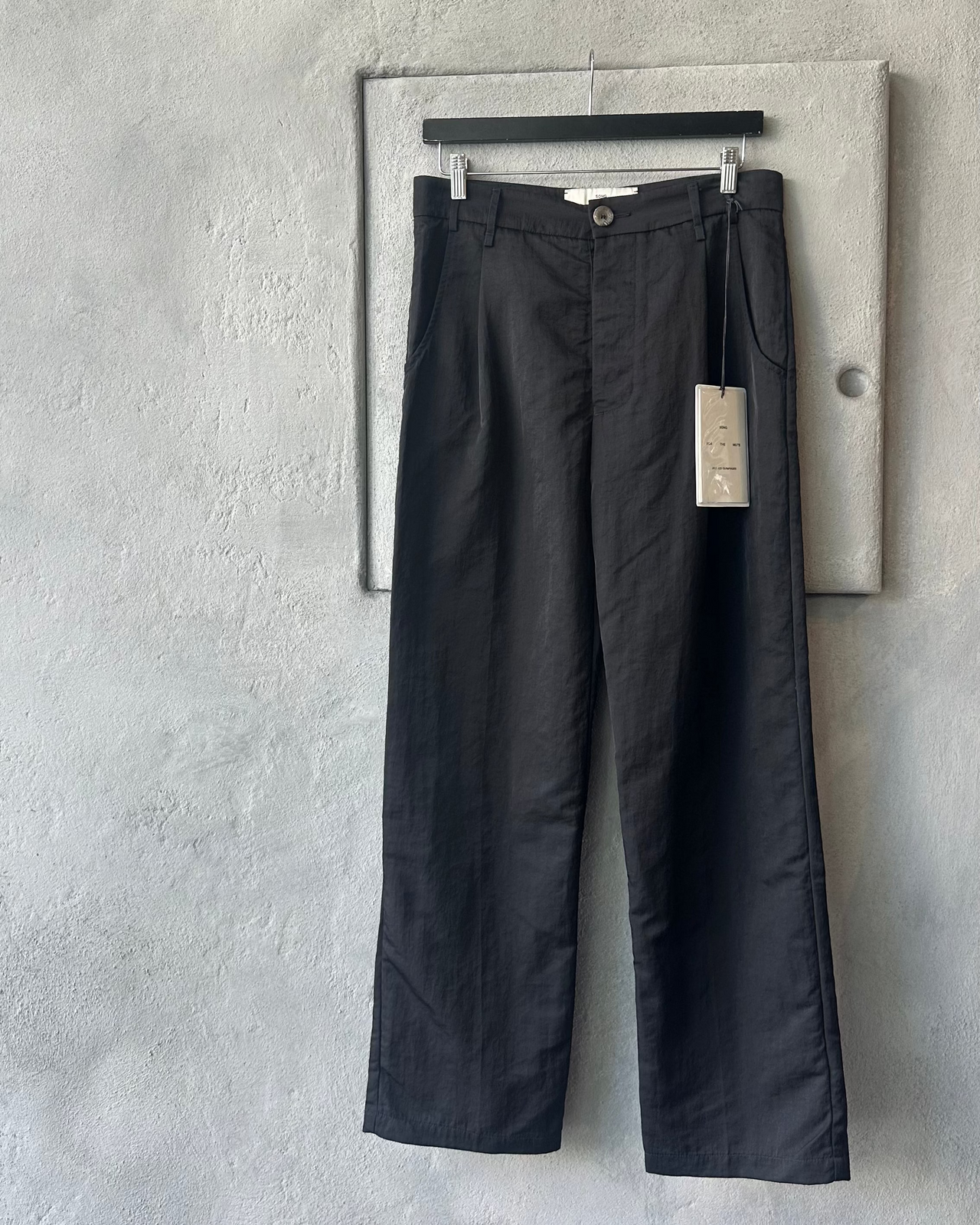Black Song For The Mute pants hanging on a rack against a gray wall