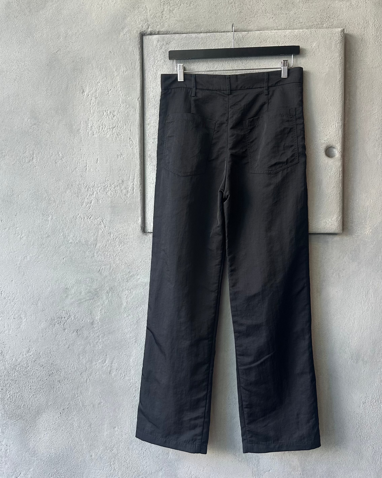 Black Song For The Mute pants hanging on a rack against a gray wall