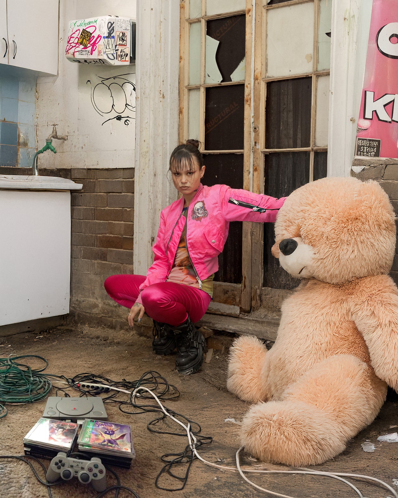 Person in a pink Unravel Project jacket interacting with a large teddy bear in a dilapidated room.