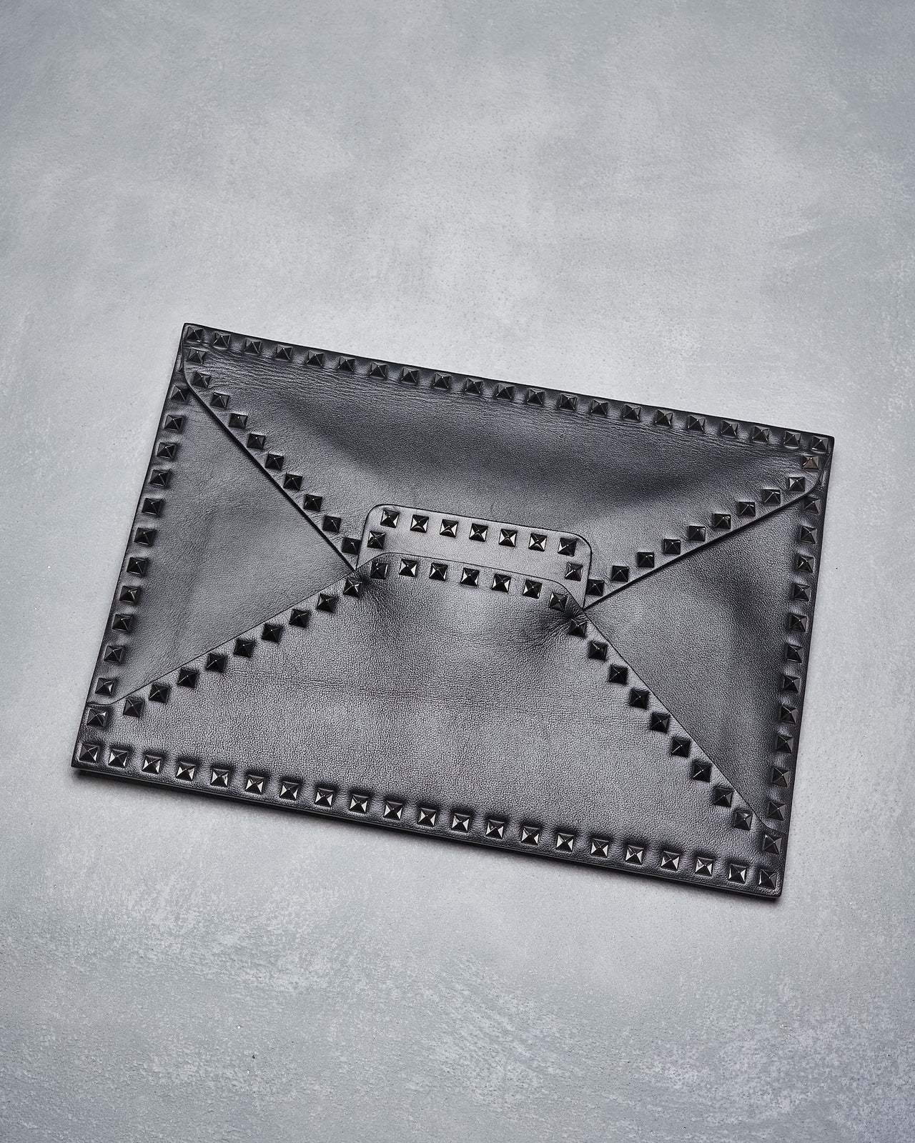 A gray leather envelope clutch with Valentino's iconic pyramid stud embellishments and a magnetised closure.