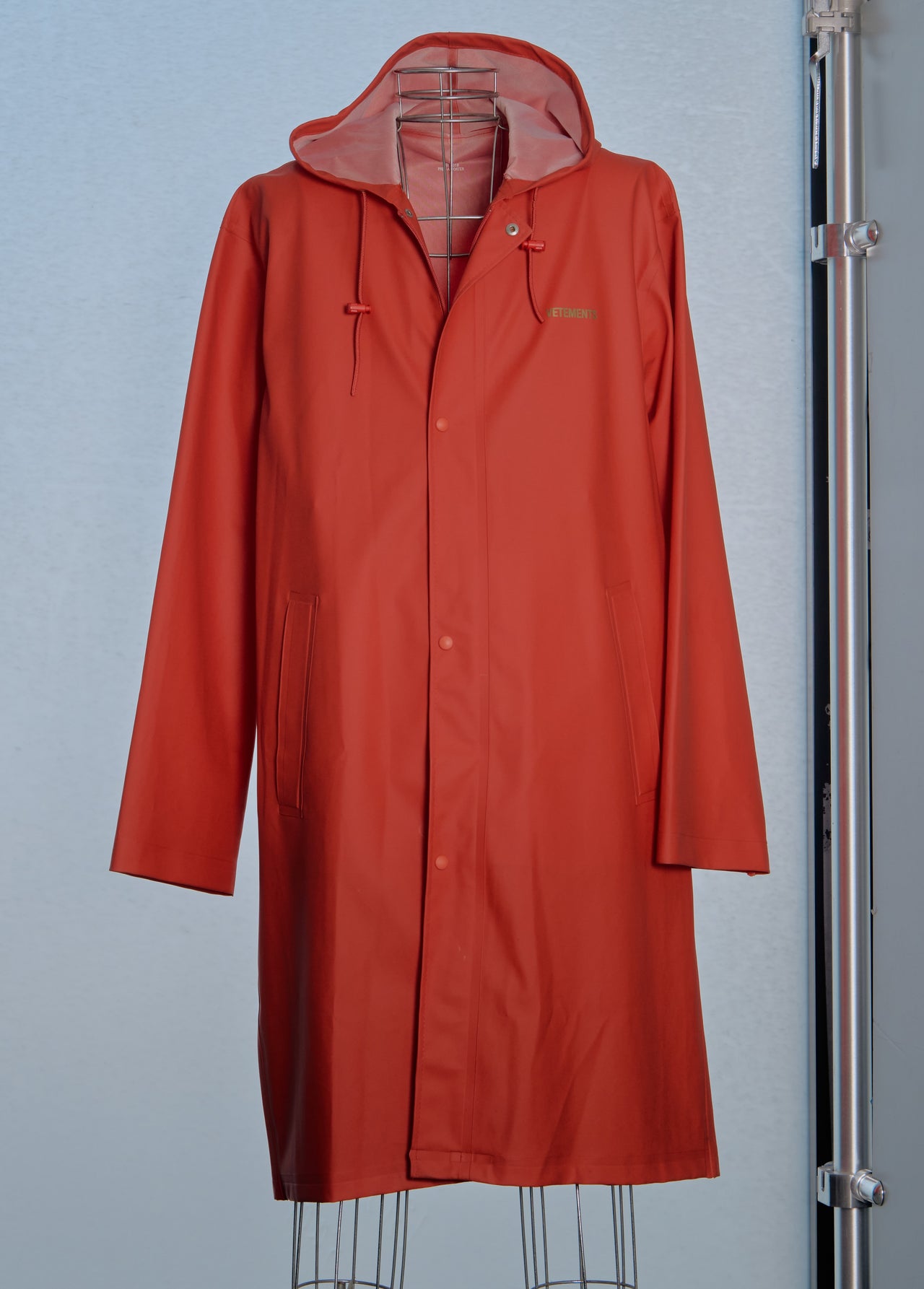 Red Vetements raincoat on a stand against a gray background