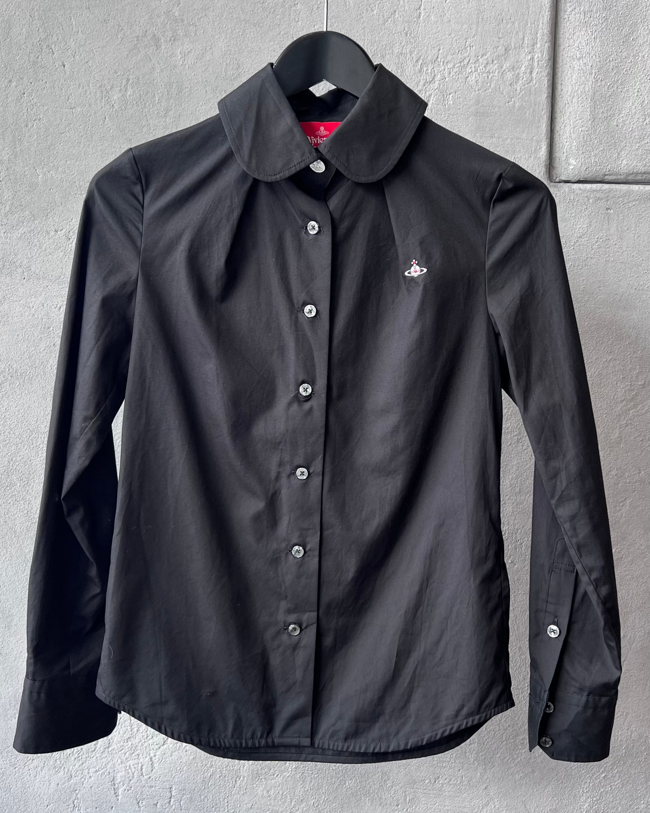 Black Vivienne Westwood shirt with a brand logo on a hanger against a gray wall