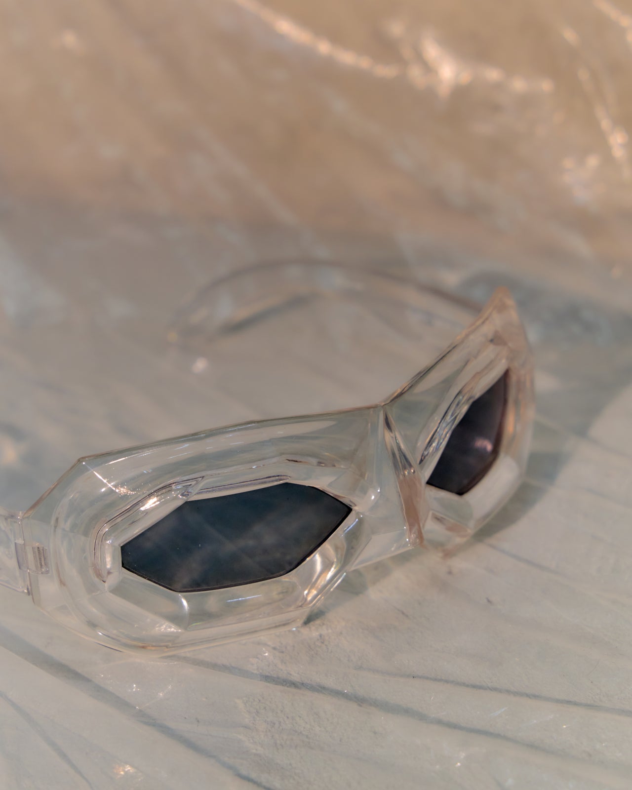 Clear Walter Van Beirendonck x Linda Farrow sunglasses with dark lenses on a reflective surface