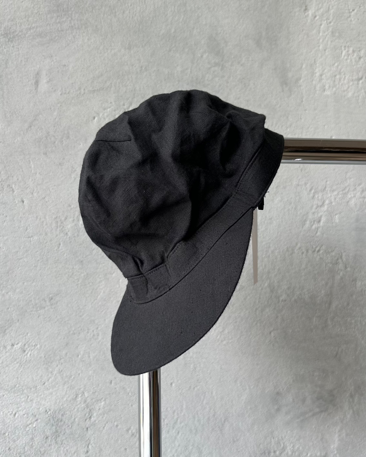 Black Y's By Yohji Yamamoto cap on a metal stand against a gray textured wall