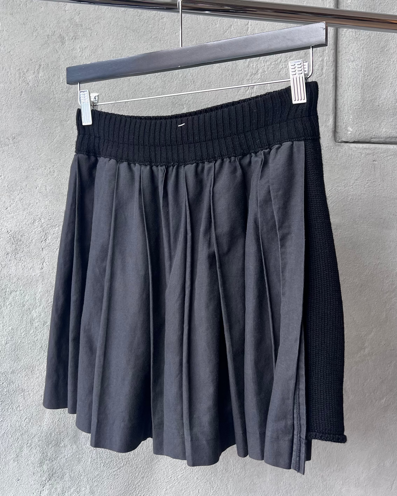 Black Y's By Yohji Yamamoto skirt hanging on a rack against a gray wall