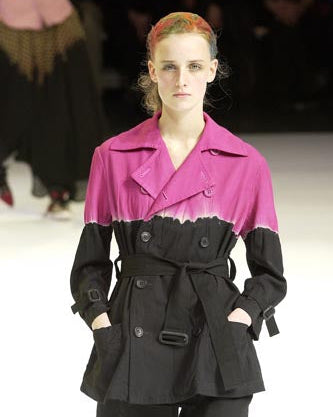 Model wearing a two-tone Y's by Yohji Yamamoto trench coat with pink and black sections on a runway.