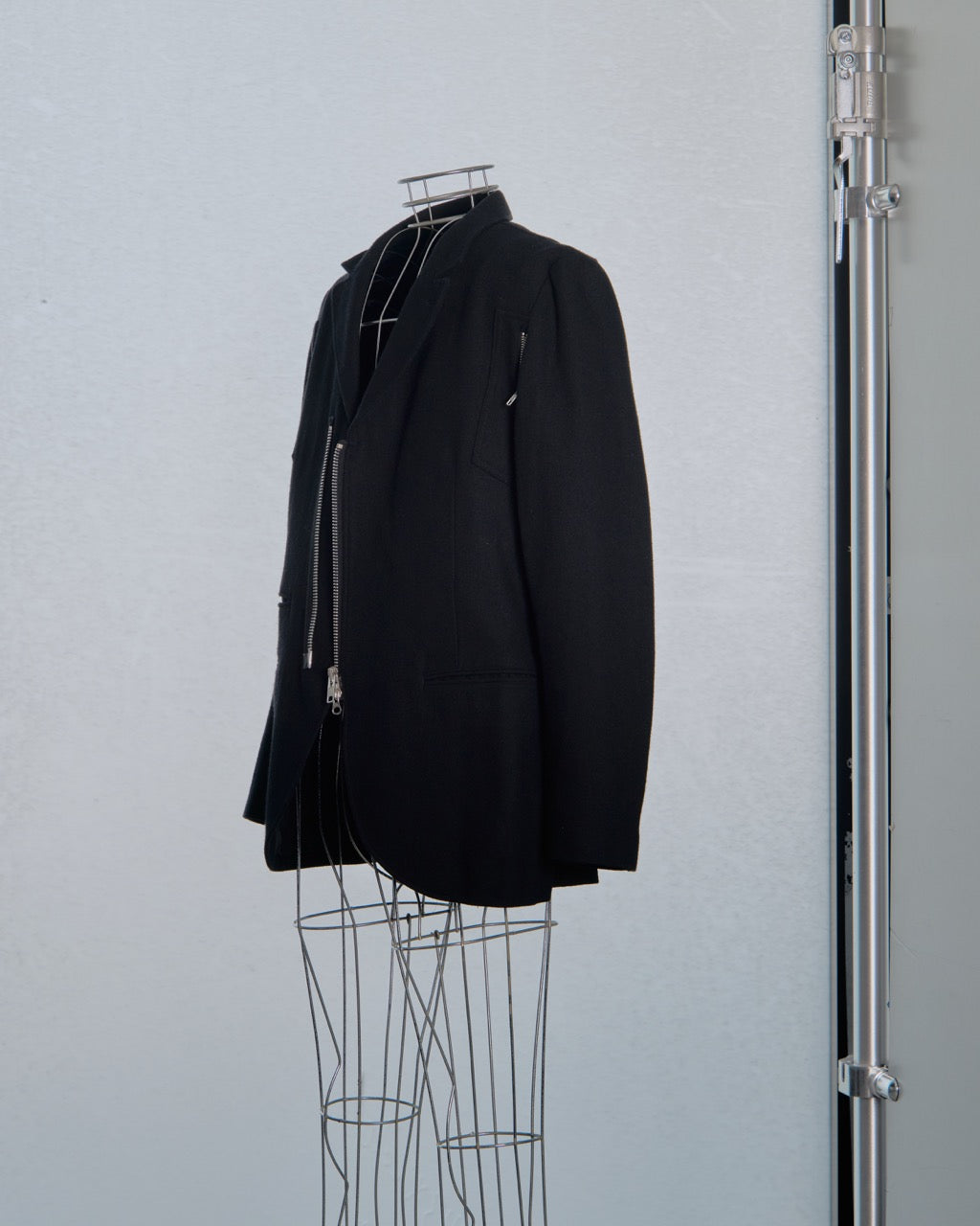 Black Yohji Yamamoto jacket with zippers on a mannequin against a gray background