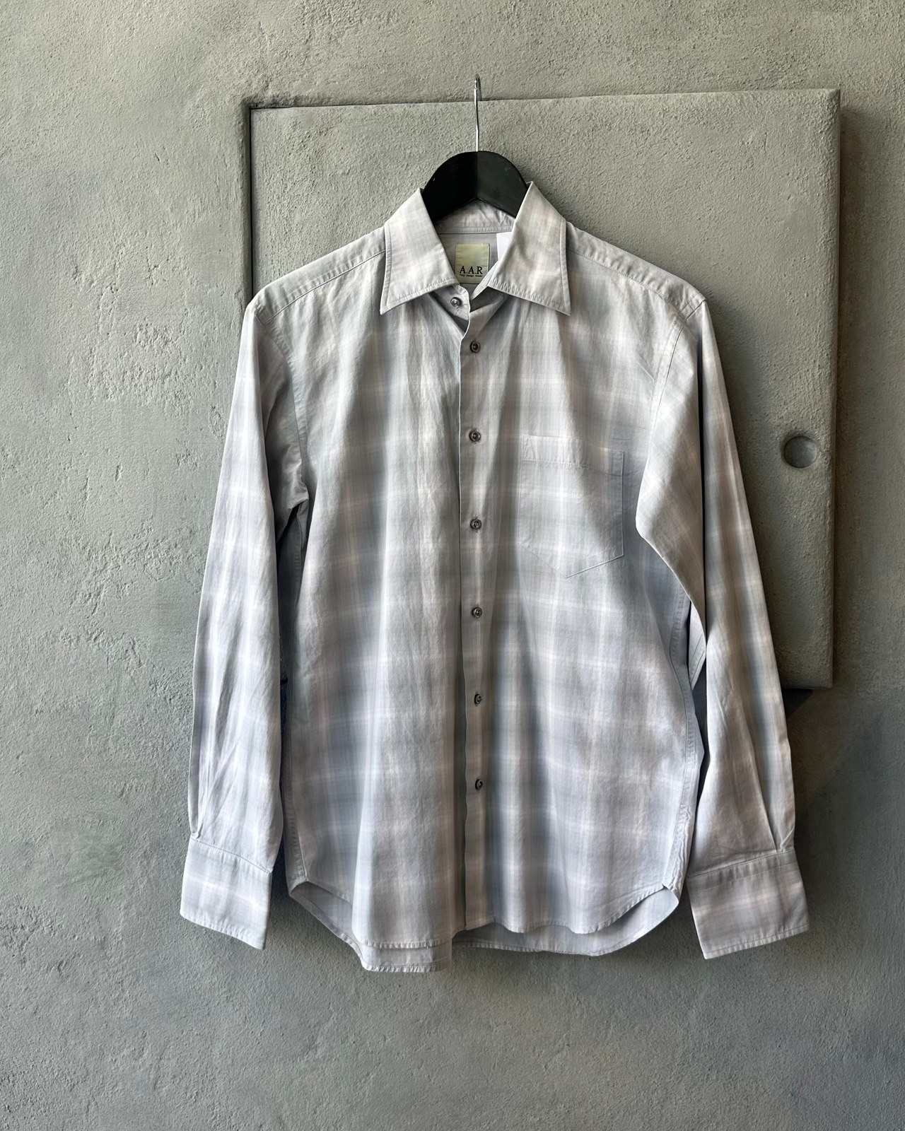 Plaid Yohji Yamamoto A.A.R shirt hanging on a hook against a concrete wall