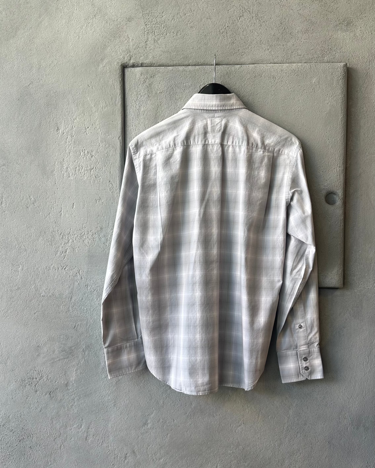 Plaid Yohji Yamamoto A.A.R shirt hanging on a hook against a concrete wall