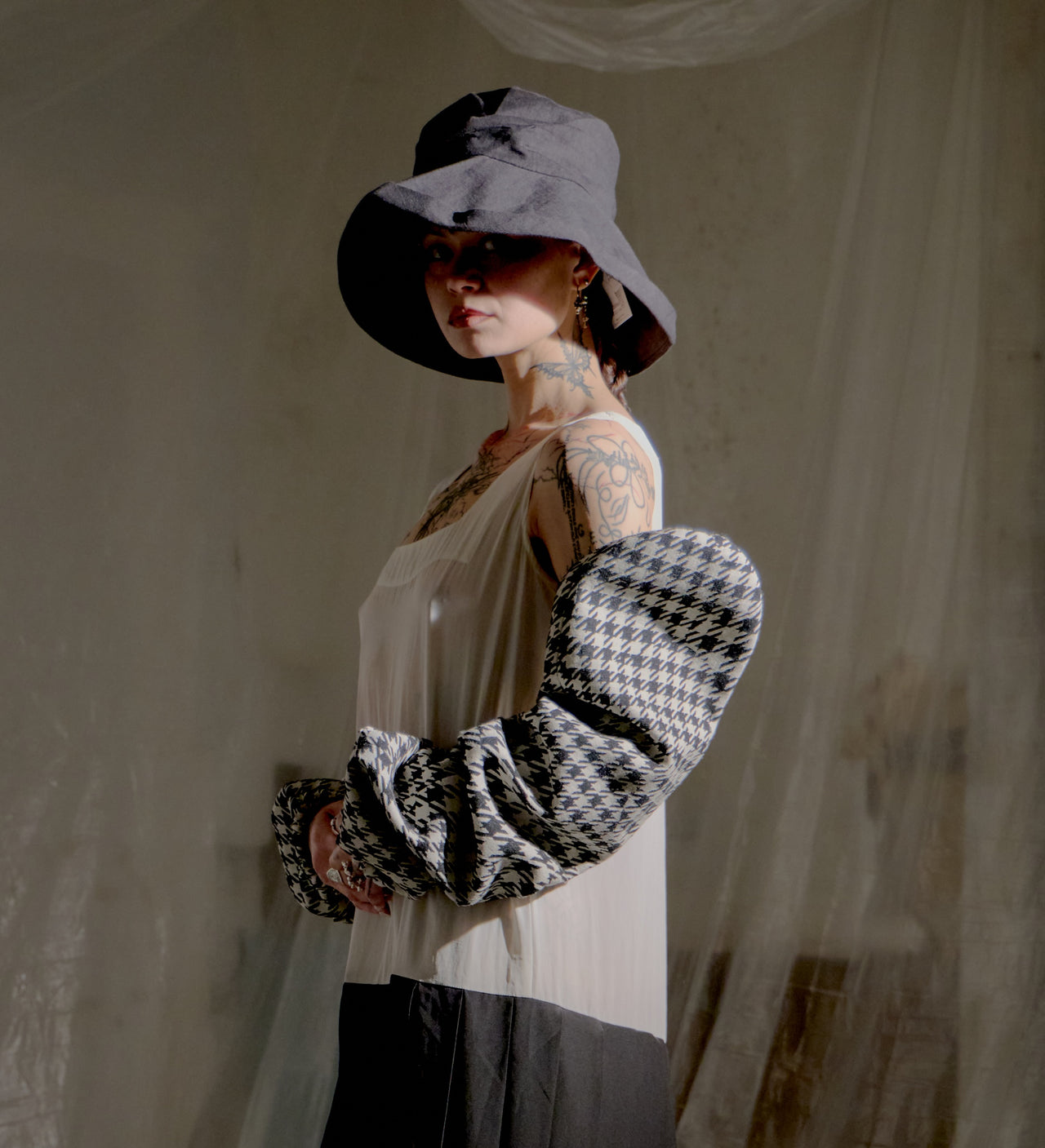 Person wearing a black and white checkered Yohji Yamamoto sleeves with a sheer top, standing against a neutral background.