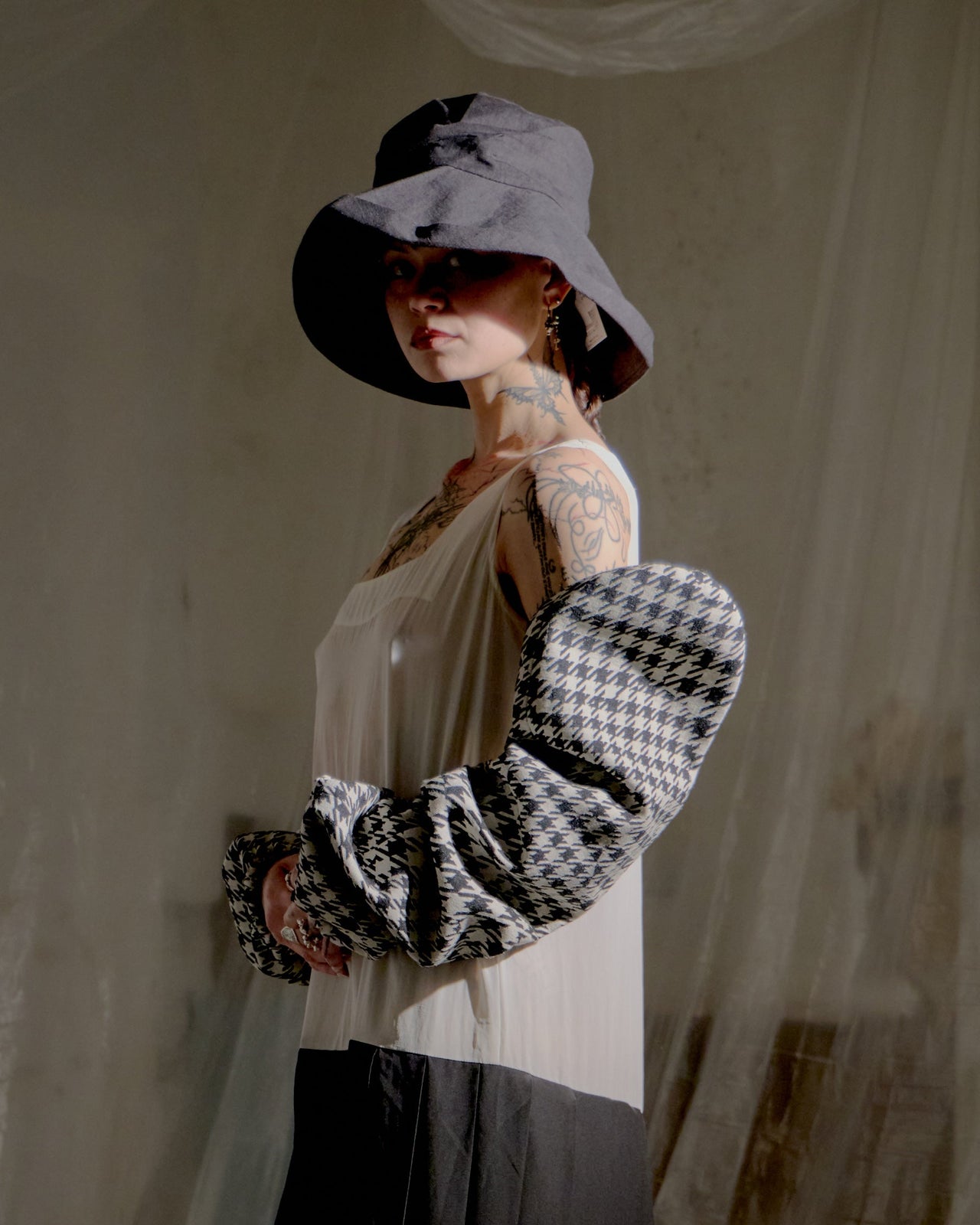 Person wearing a black and white checkered Yohji Yamamoto sleeves with a sheer top, standing against a neutral background.