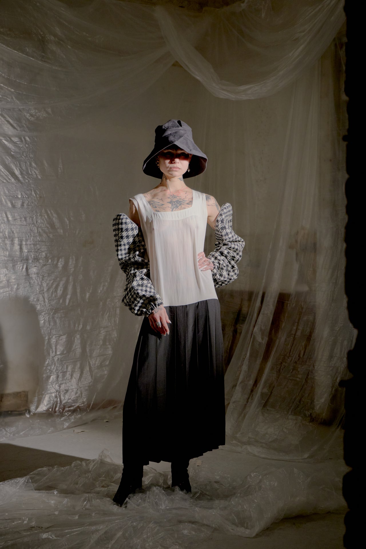 Person wearing a black and white checkered Yohji Yamamoto sleeves with a sheer top, standing against a neutral background.