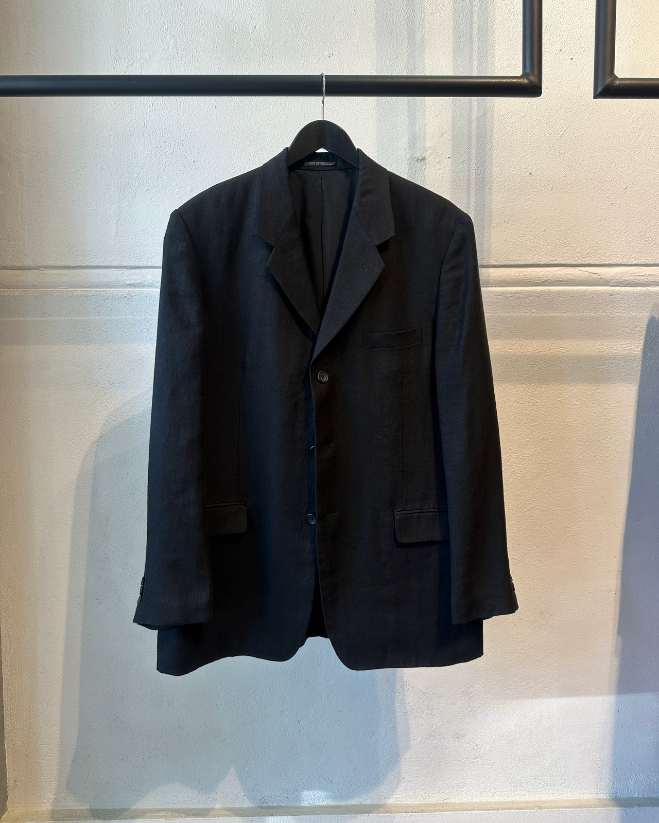 Black Yohji Yamamoto jacket hanging on a rack against a neutral background