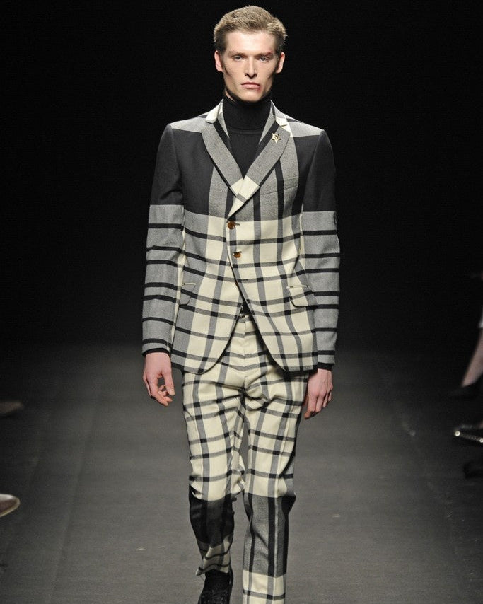 Model wearing a checkered Vivienne Westwood suit with a black turtleneck on a runway.