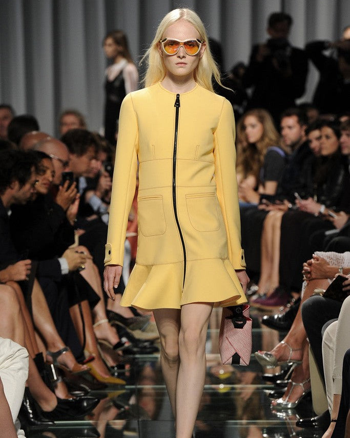 Model wearing a yellow Louis Vuitton cruise outfit on a fashion runway with an audience.