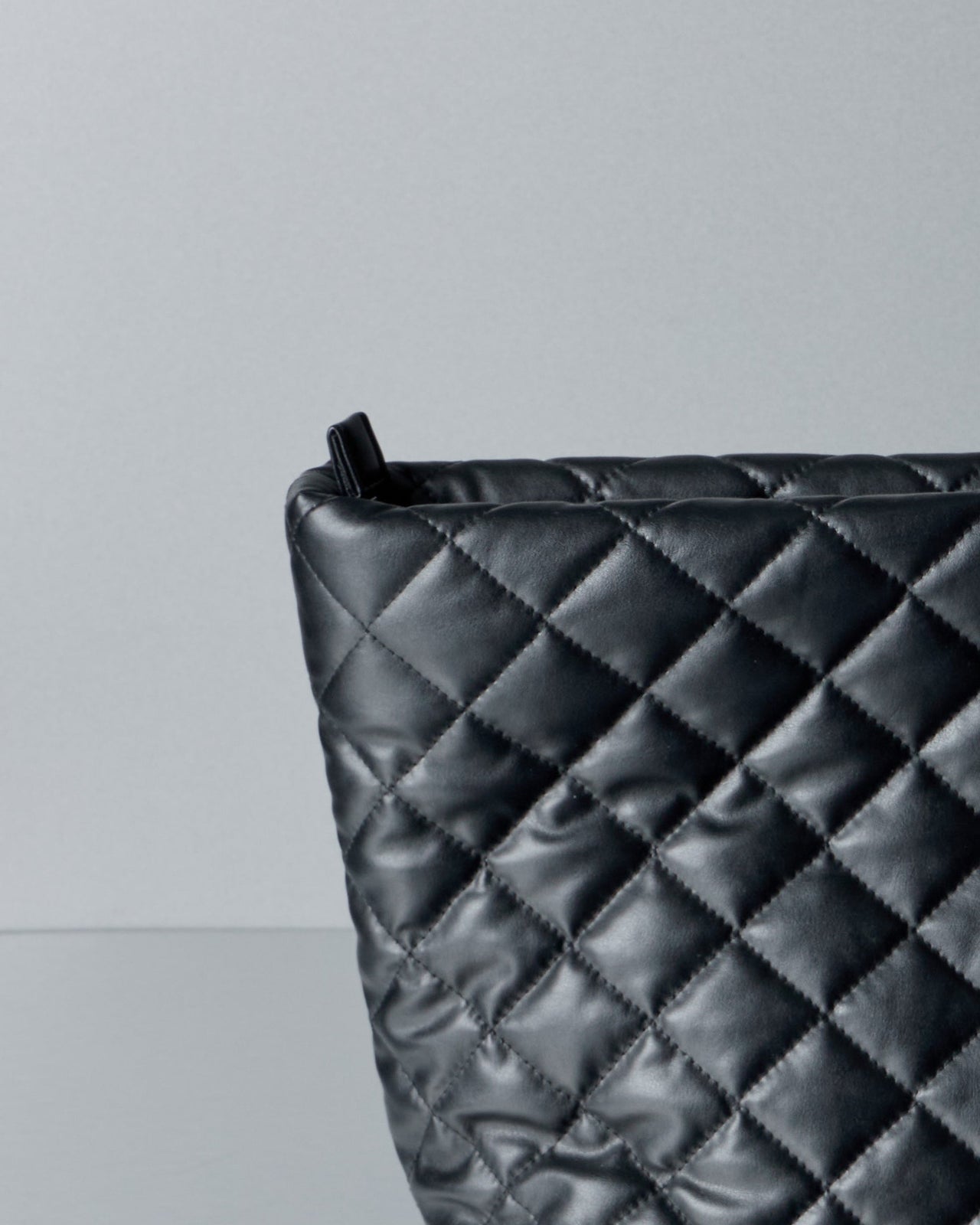Black quilted Comme des Garcons Junya Watanabe handbag on a gray background