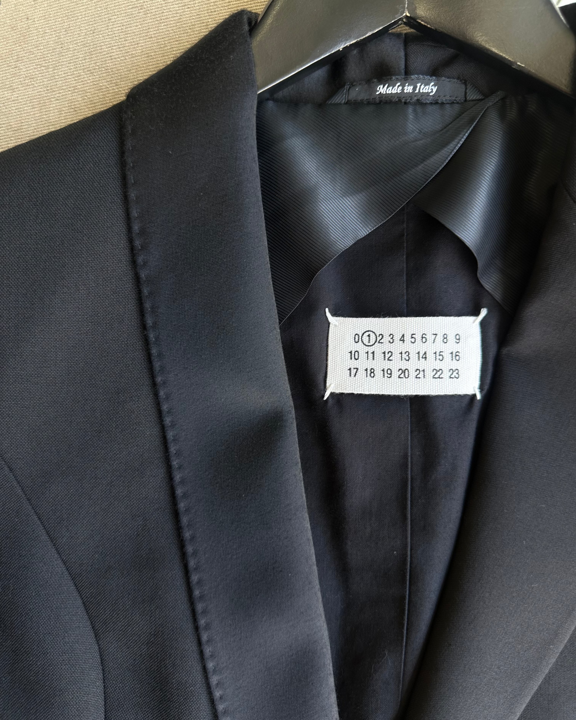 Black Maison Margiela suit jacket with a tag on a beige background