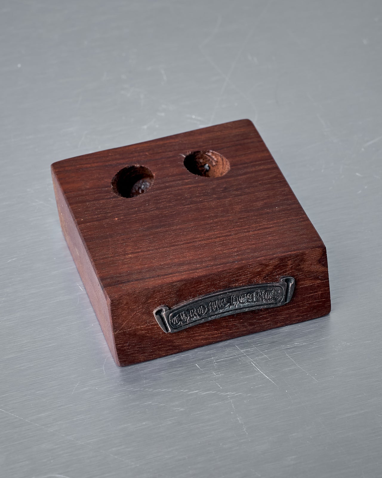 Wooden block with two holes and a metal logo plaque on the front