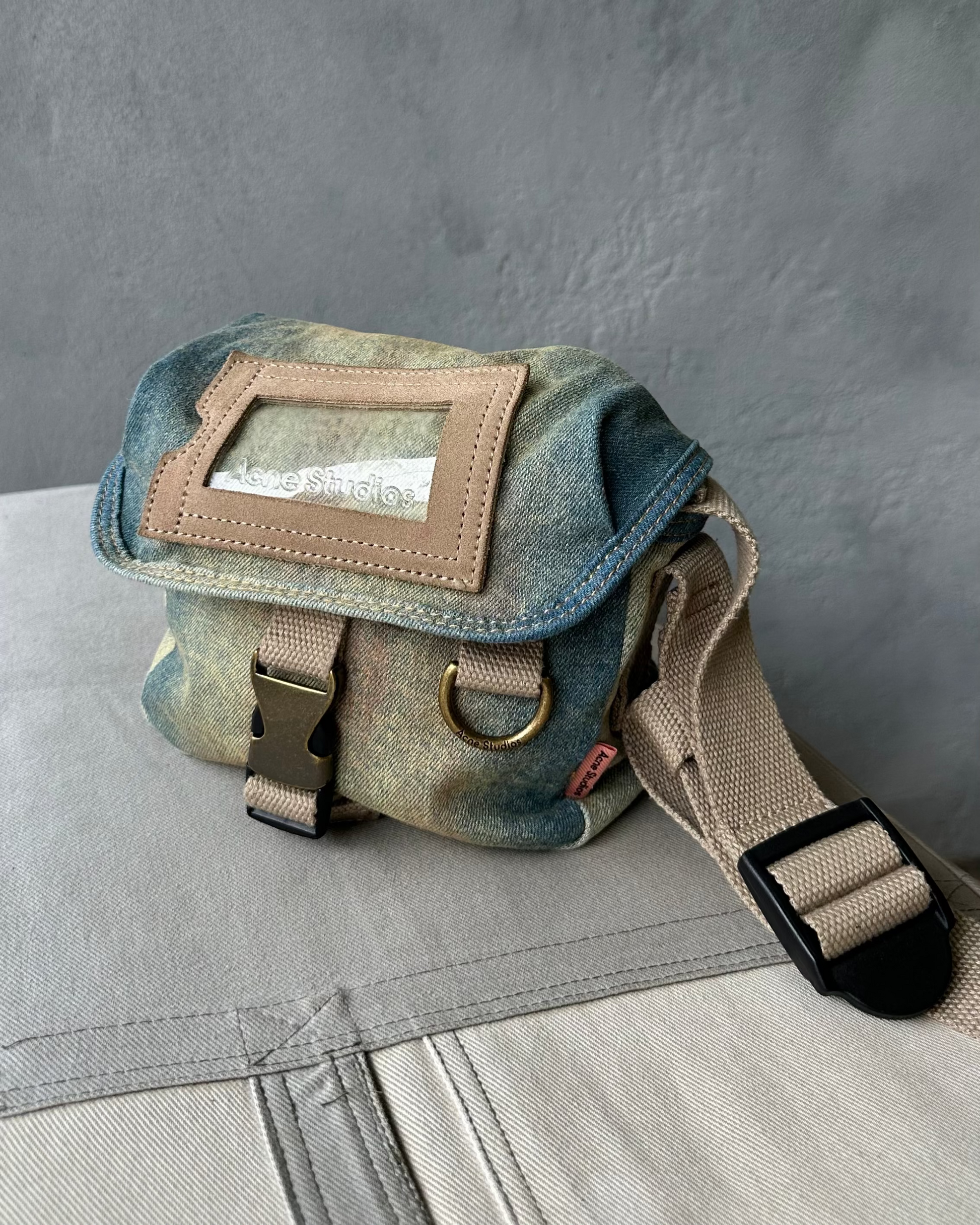 Small Denim Acne Studios bag with a strap on a gray surface