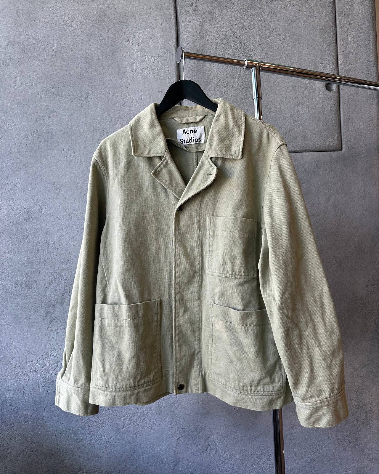 Beige Acne Studios jacket on a hanger against a gray wall