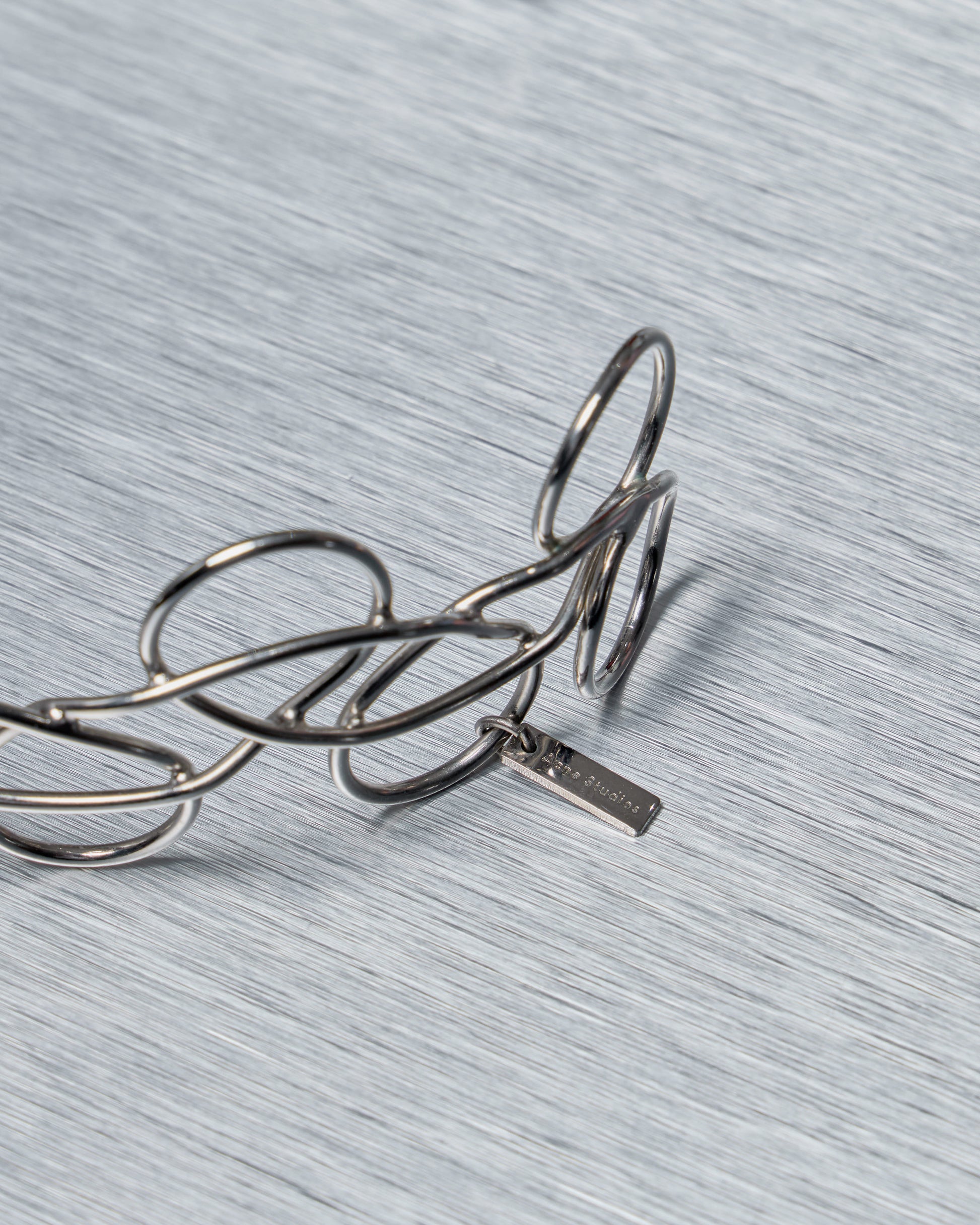 Close up of an Acne Studios chocker necklace in silver on a textured gray surface